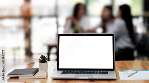 Photo of computer laptop with white blank screen putting on the modern working table with business people having a blurred meeting in the background.