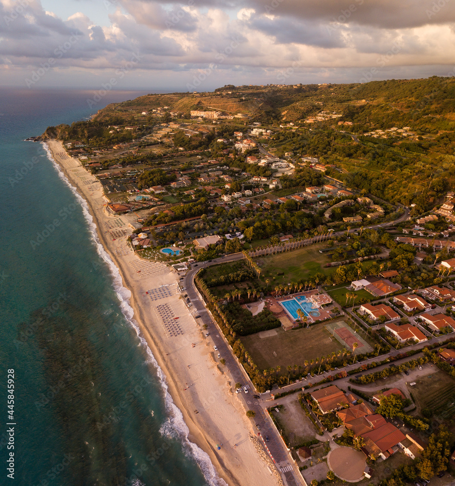 Aerial view of a sunset over the sea in Zambrone, coast of Calabria. Italy. Houses and trees near the beach with umbrellas. Tourist resorts and holidays