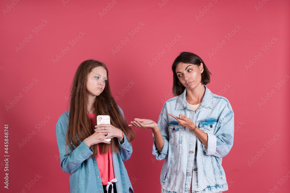 Modern mom and daughter in denim jackets on terracotta background, girl with phone and mom stands by trying to take phone Modern mom and daughter in denim jackets on terracotta background, girl with phone and mom stands by trying to take phone