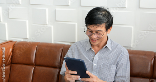 Senior Asian man playing tablet and video call on sofa in living room at home Portrait of Asian elderly man is Relaxing and Happiness With playing tablet
