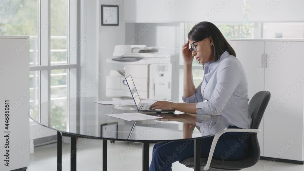 Focused young businesswoman sitting at desk and using laptop in modern office. Focused young businesswoman sitting at desk and using laptop in modern office.