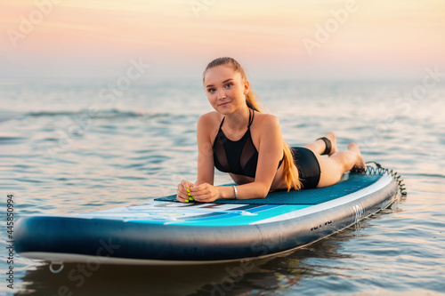 Surfing. Pretty fit girl lying on a sup board at ocean surface. In the background, the ocean and the sunset. Summer activity and extreme recreation