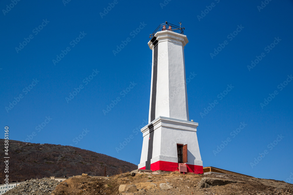 Lighthouse (leading beacon) on the sea coast. White lighthouse against the blue sky. Marine navigation and infrastructure.