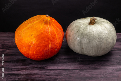 two pumpkins of different colors on a wooden table