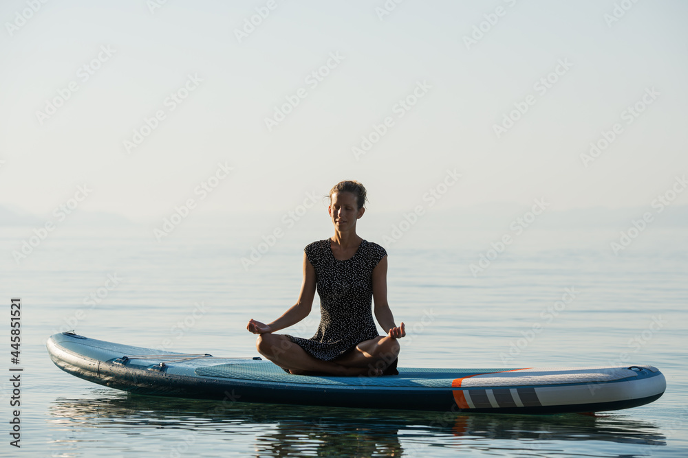 Young woman meditating in peace on a sup board