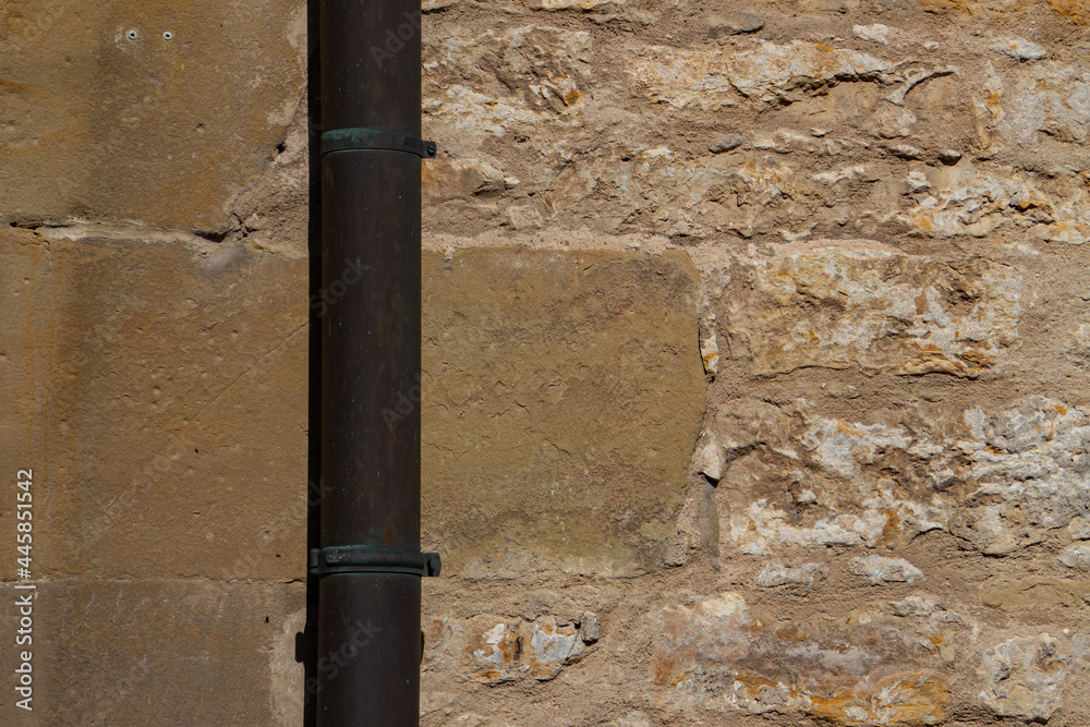Downpipe in front of a sandstone and natural stone wall with copy space Downpipe in front of a sandstone and natural stone wall with copy space