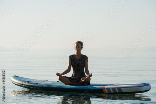Young woman meditating in peace on a sup board © Gajus