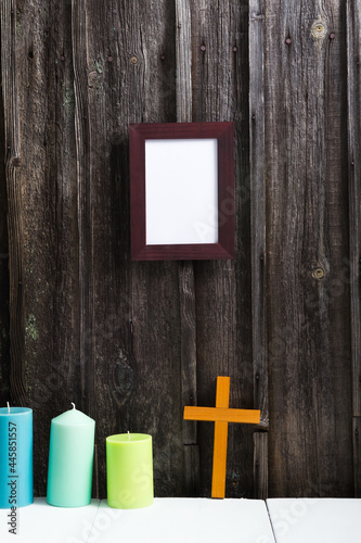 empty picture frame, cross and candles on white table, old weathered wooden wall background