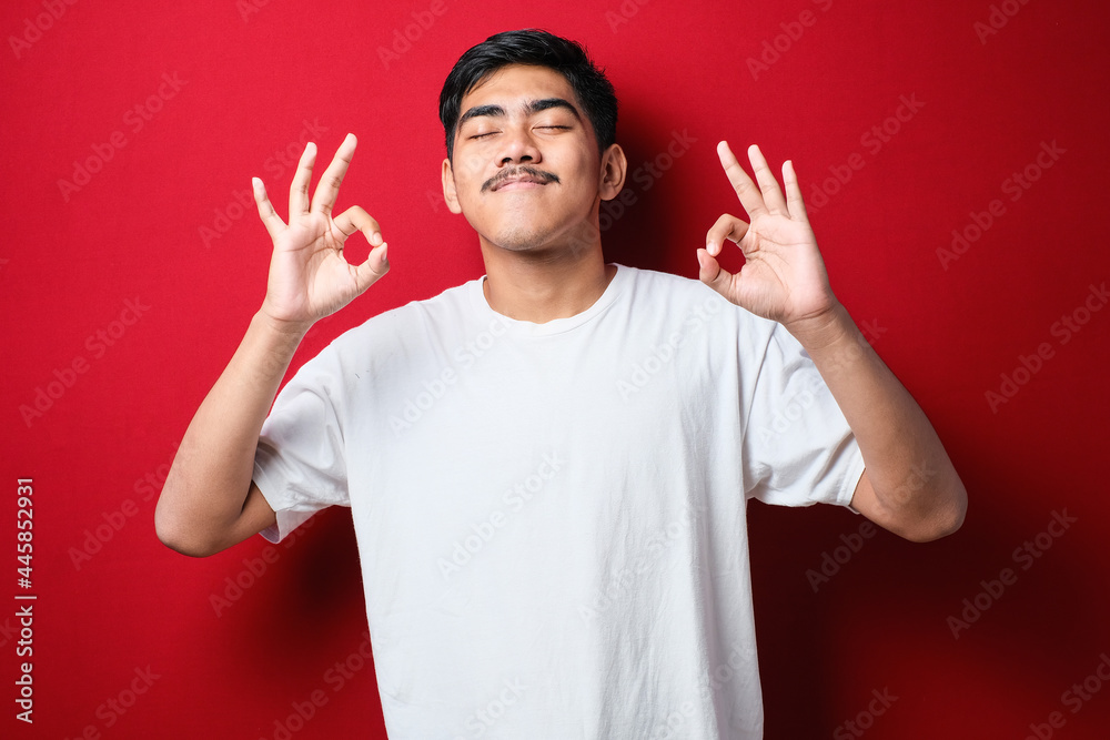 Young indian man wearing casual shirt relax and smiling with eyes closed doing meditation gesture with fingers. Yoga concept. Young indian man wearing casual shirt relax and smiling with eyes closed doing meditation gesture with fingers. Yoga concept.