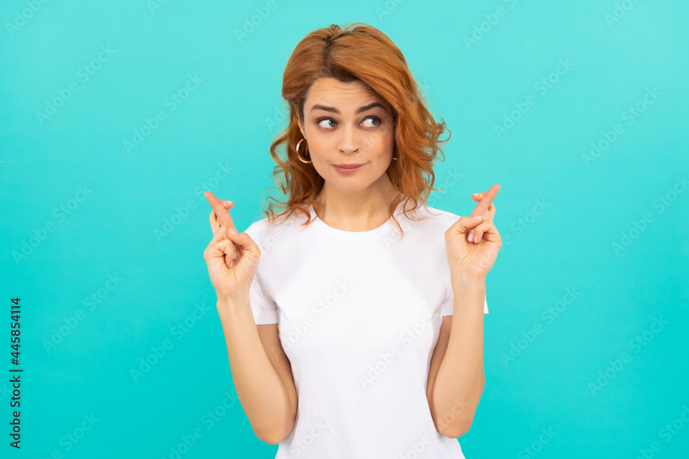 dreamy redhead girl with curly hair cross fingers making a wish on blue background, dream dreamy redhead girl with curly hair cross fingers making a wish on blue background, dream