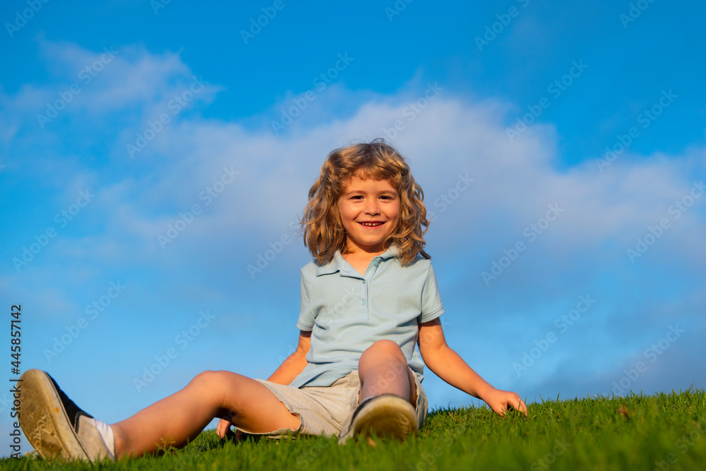 Happy child boy sitting on green grass outdoors in spring park. Happy child boy sitting on green grass outdoors in spring park.