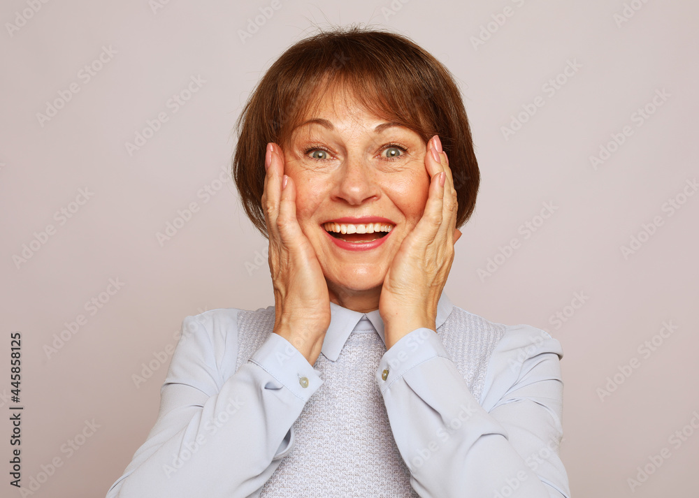 Life only starts when get older. Portrait of happy and charming european senior woman with short hair laughing and amusement holding palms on cheeks Life only starts when get older. Portrait of happy and charming european senior woman with short hair laughing and amusement holding palms on cheeks