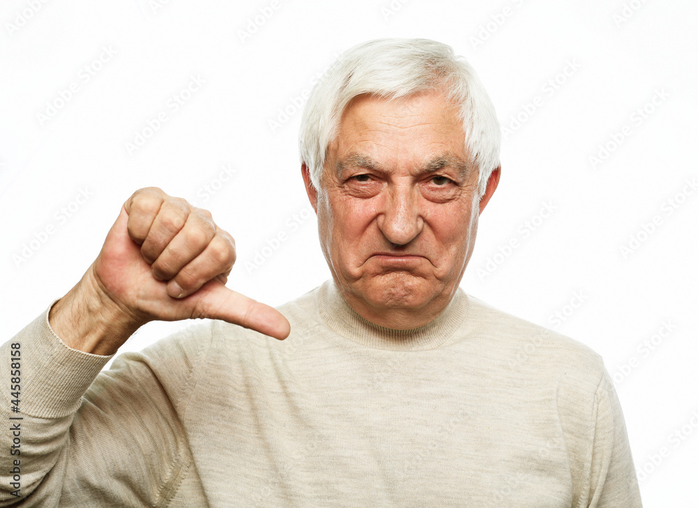 Senior man standing over isolated white background looking unhappy and angry showing rejection and negative with thumbs down gesture.