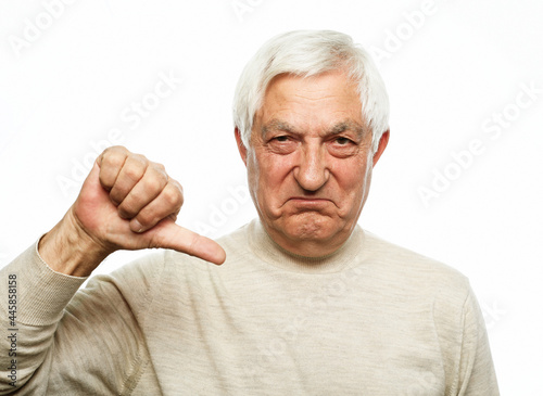 Senior man standing over isolated white background looking unhappy and angry showing rejection and negative with thumbs down gesture.