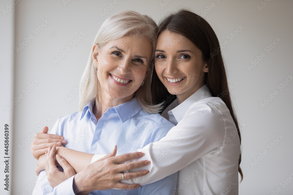 Happy young grownup daughter hugging mature mother, looking at camera, smiling, Affectionate cheerful millennial girl embracing senior 60s grandma. Family relationship concept. Head shot portrait Happy young grownup daughter hugging mature mother, looking at camera, smiling, Affectionate cheerful millennial girl embracing senior 60s grandma. Family relationship concept. Head shot portrait