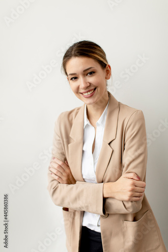Young woman looking like a happy, proud and satisfied achiever, smiling with arms crossed against white wall