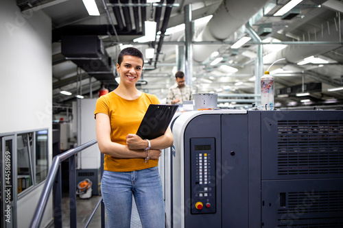 Portrait of talented female designer standing by modern printing machine in print shop. photo