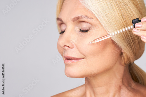 Close-up of a mature lady applies face serum.