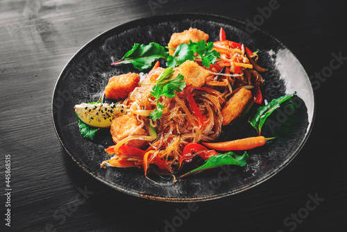 asian noodles with fried cheese tofu and vegetables in plate on black wooden table background