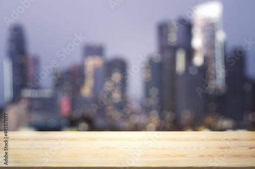 Empty wooden table top with beautiful blurry skyscrapers at evening on background  mock up