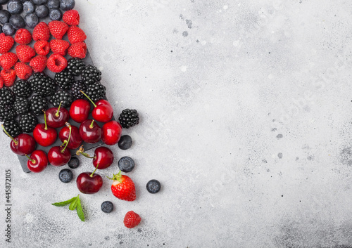Fresh organic summer berries mix on black marble board on light kitchen table background. Raspberries, strawberries, blueberries, blackberries and cherries. Space for text