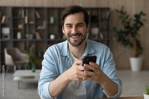 Portrait of smiling young man holding smartphone in hands, addicted to modern technology millennial guy using cellphone applications, enjoying spending time online, communicating distantly or shopping