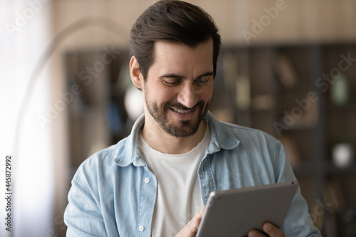 Head shot happy millennial generation man using touchpad indoors, typing message, checking email, communicating distantly in social network, web surfing information or shopping in internet store.