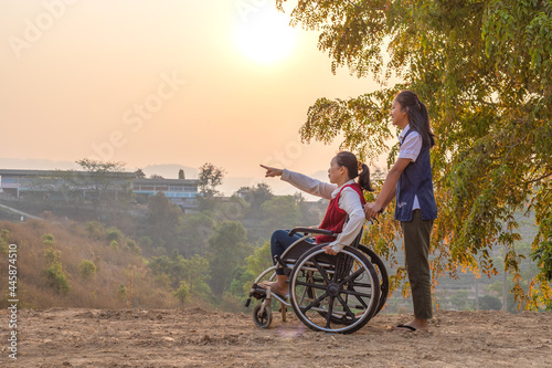 Disabled handicapped woman in wheelchair and care helper walking in park.