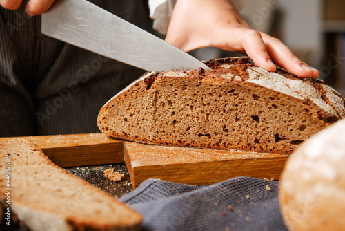 cuts rye bread with a knife on a board
