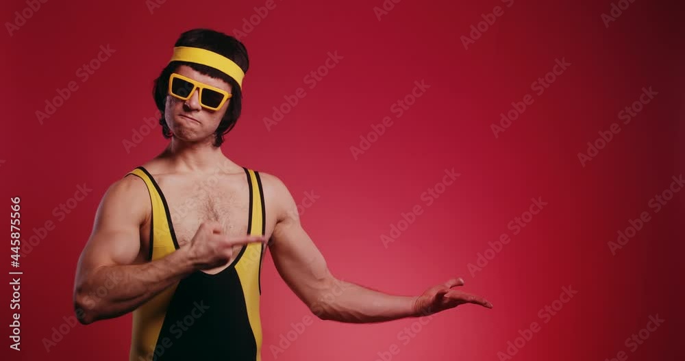 Funny retro hipster athlete man in yellow tracksuit and sunglasses from 80's show and represent product logo by his hands on a copy space isolated on red background. Promotion commercial concept