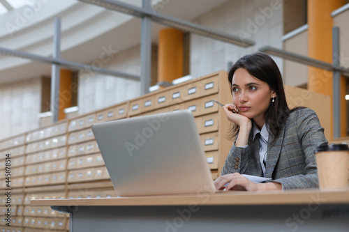 Portrait of a pretty female student with laptop in library.