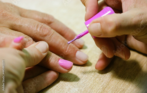 Manicurist applies pink gel shellac nail polish on client s nails  beauty salon.