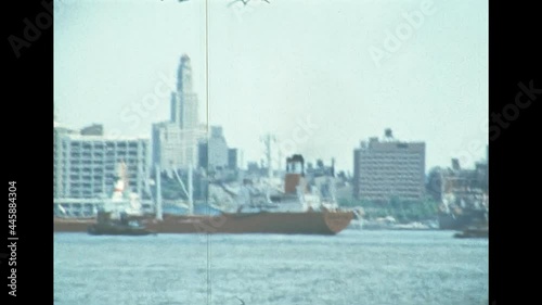 Cargo ship in the Manhattan pier by the old skyline of New York city. United States America in 1976. Archival of Manhattan downtown skyline from Hudson river by sightseeing cruise.