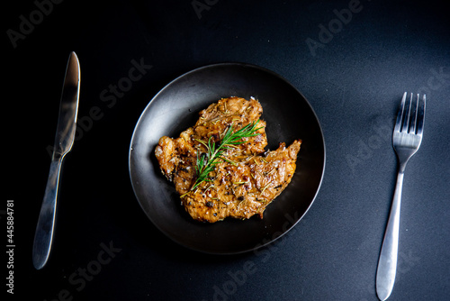 Steak on the plate and black background sprinkled with salt and pepper. 