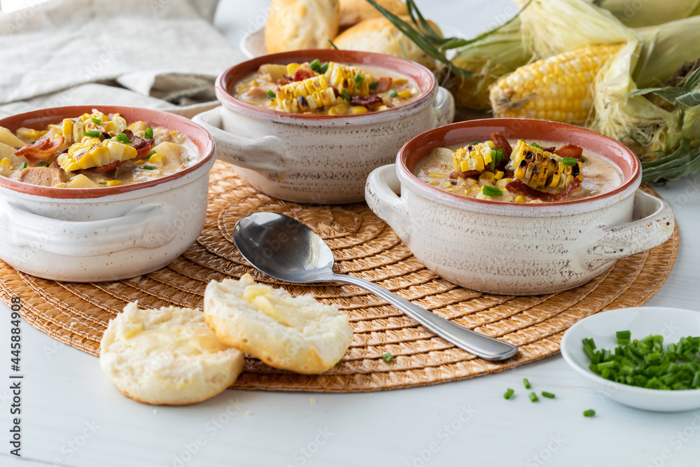 Close up view of soup crocks filled with chicken and corn chowder garnished with grilled corn, bacon and chives. Close up view of soup crocks filled with chicken and corn chowder garnished with grilled corn, bacon and chives.