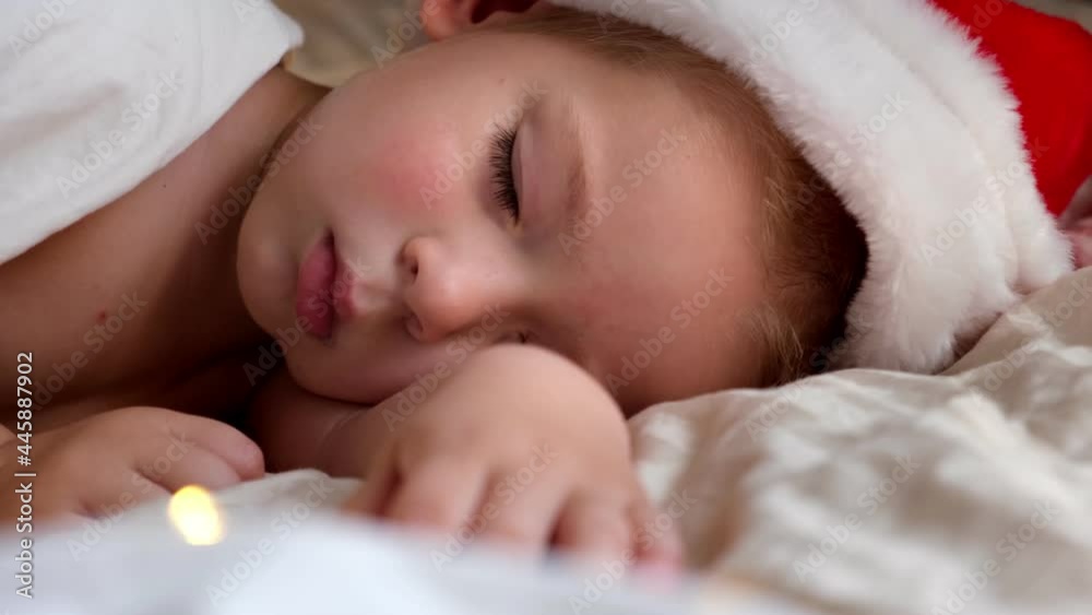 Cute Sleeping Boy in Santa Claus Hat Lying in Bed at Home. Christmas Light. Xmas, New Year Winter Holiday Concept. Dream. Child sleeping before Christmas. Cute Sleeping Boy in Santa Claus Hat Lying in Bed at Home. Christmas Light. Xmas, New Year Winter Holiday Concept. Dream. Child sleeping before Christmas.