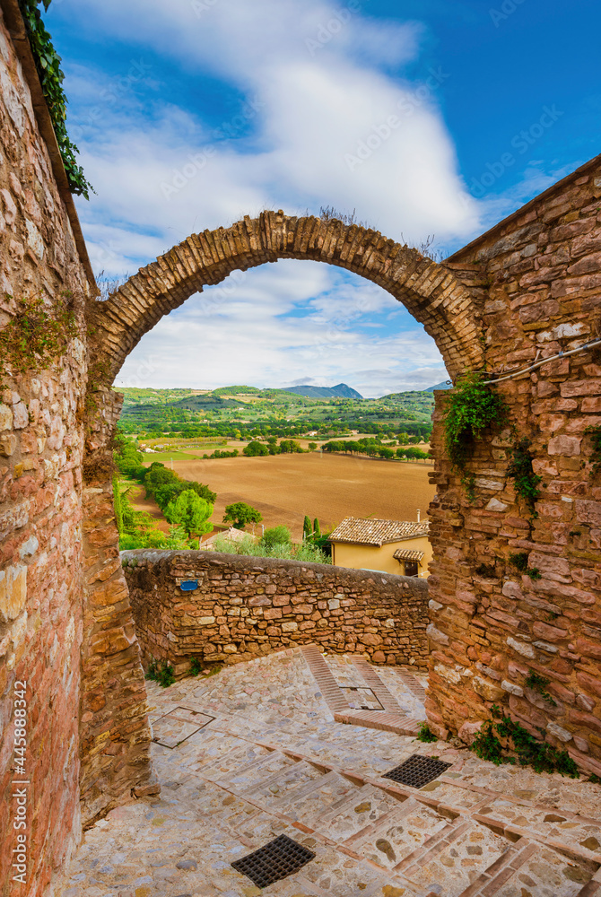 Spello charming historic center lane with stone arch and Umbria countryside beautiful view