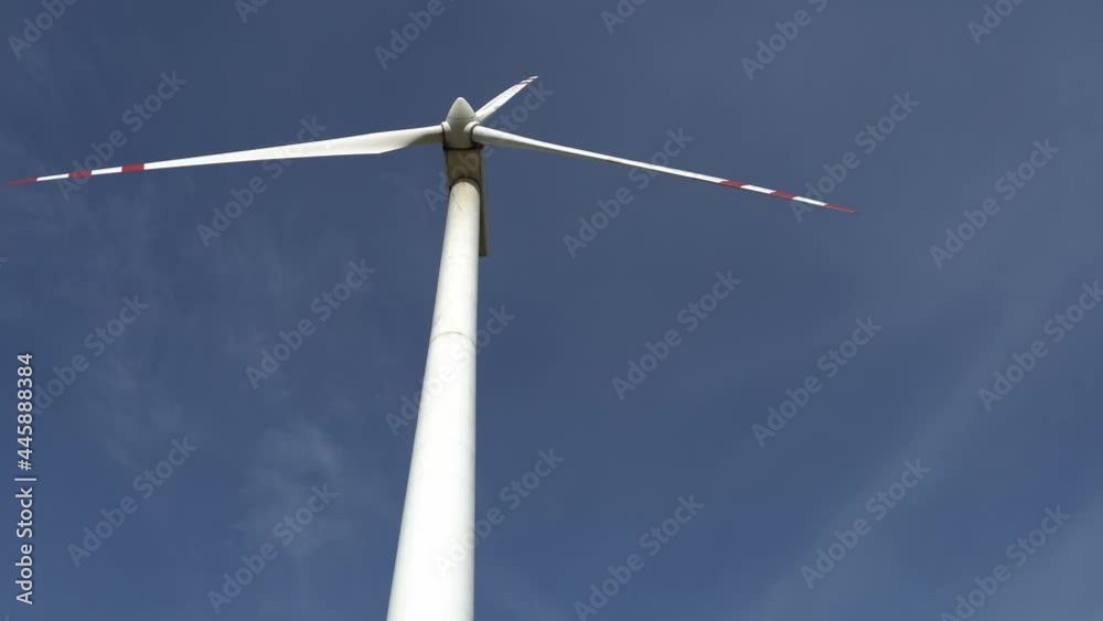 view of a modern windmill against a blue sky. The white blades of the wind turbine close up. Renewable energy source. Production of cheap and safe electricity. view of a modern windmill against a blue sky. The white blades of the wind turbine close up. Renewable energy source. Production of cheap and safe electricity.