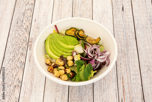 Vegetable salad with coriander, chopped ripe avocado, red onion, roasted cucumbers, whole hazelnuts and lettuce sprouts inside a bowl for home delivery