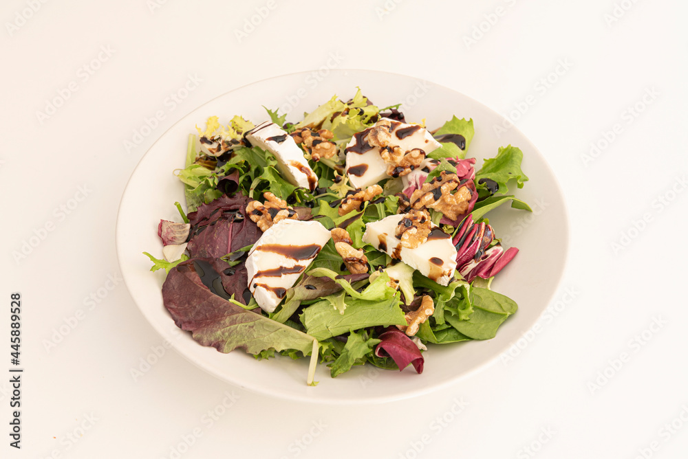 chopped goat cheese salad, assorted lettuce sprouts, peeled and split California walnuts, balsamic vinegar and white plate on a white background