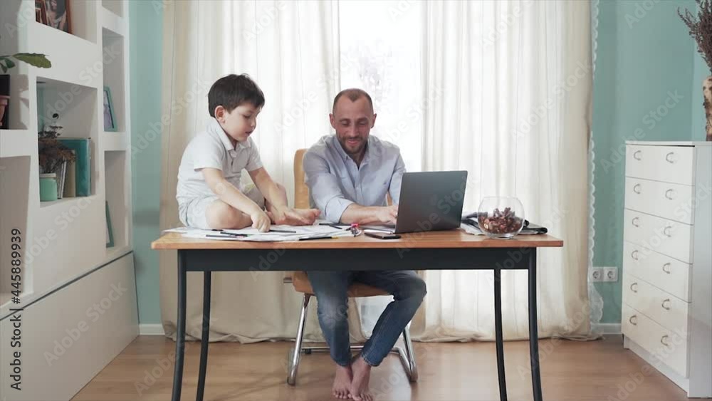 Parent working online from home. SLOW MOTION. Remote work. Family on self-isolation. Home office. Dad and son enjoy their time together. They give each other fives. Paternity. Quarantine. Epidemic Parent working online from home. SLOW MOTION. Remote work. Family on self-isolation. Home office. Dad and son enjoy their time together. They give each other fives. Paternity. Quarantine. Epidemic