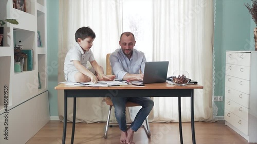 Parent working online from home. SLOW MOTION. Remote work. Family on self-isolation. Home office. Dad and son enjoy their time together. They give each other fives. Paternity. Quarantine. Epidemic