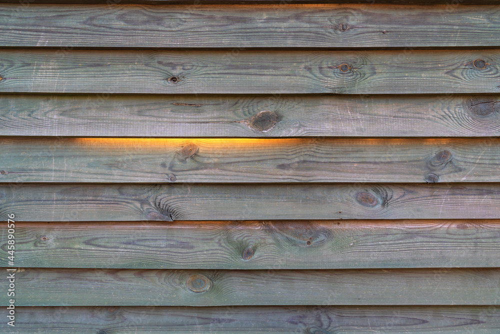 Fototapeta premium Fragment of a dark brown wooden fence. It looks like a blind. The wood texture is visible on the boards. Sunlight shines through the cracks from the other side. Background.