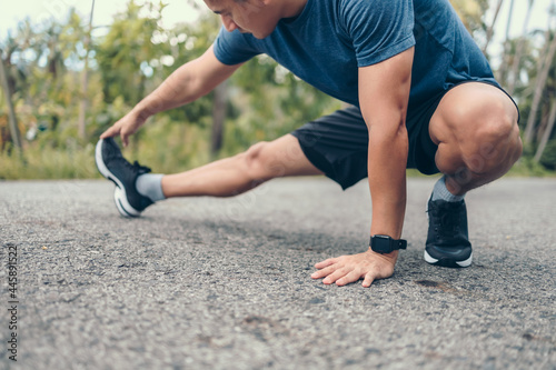 young man stretching in the park before running. Young man workout before fitness training at the park. Healthy and exercise young man warming up on the road in the forest.