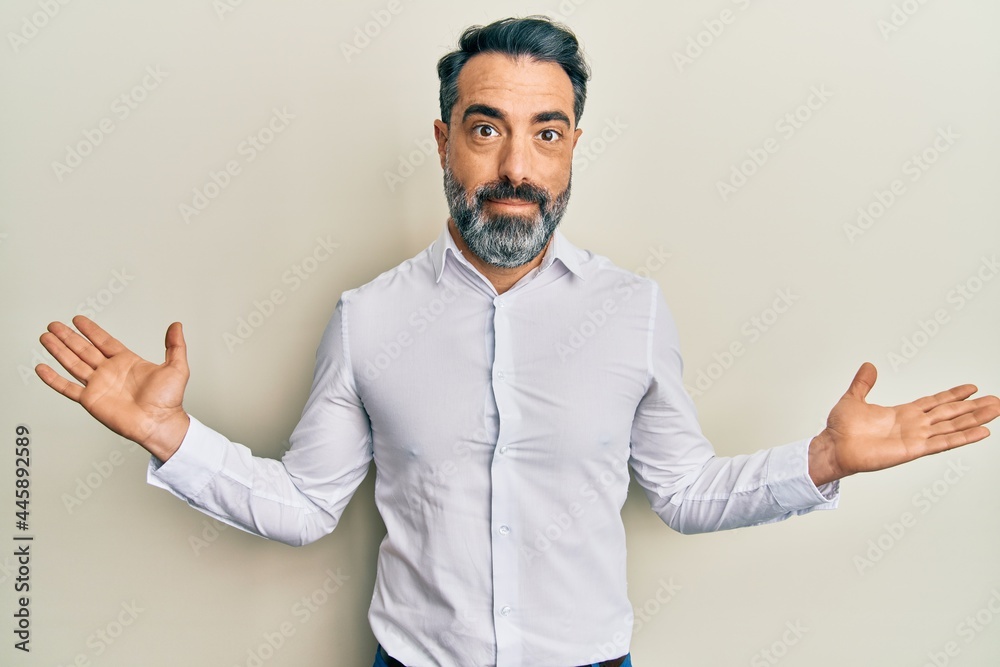 Middle age man with beard and grey hair wearing casual white shirt clueless and confused with open arms, no idea and doubtful face. Middle age man with beard and grey hair wearing casual white shirt clueless and confused with open arms, no idea and doubtful face.