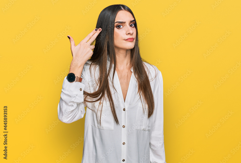 Young beautiful woman wearing casual white shirt shooting and killing oneself pointing hand and fingers to head like gun, suicide gesture. Young beautiful woman wearing casual white shirt shooting and killing oneself pointing hand and fingers to head like gun, suicide gesture.