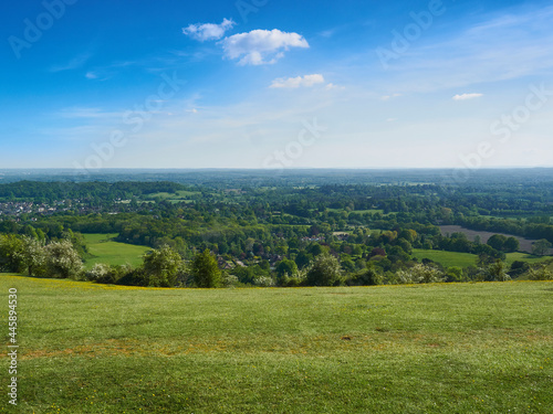 An expansive, summery, sunlit sweep of clouded blue sky, grassy green hill and the towns, fields and woodland off a Surrey valley.