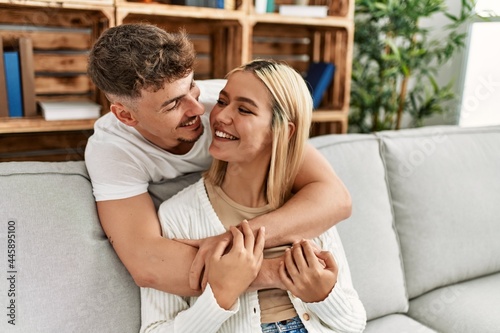 Young caucasian couple smiling happy and hugging sitting on the sofa at home.