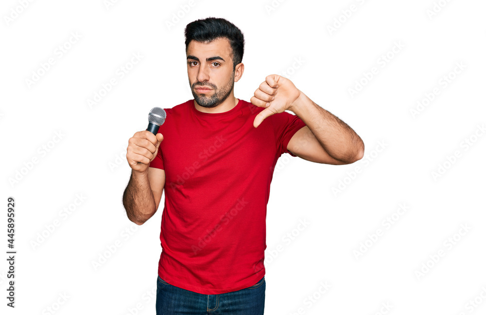 Hispanic man with beard singing song using microphone with angry face, negative sign showing dislike with thumbs down, rejection concept Hispanic man with beard singing song using microphone with angry face, negative sign showing dislike with thumbs down, rejection concept