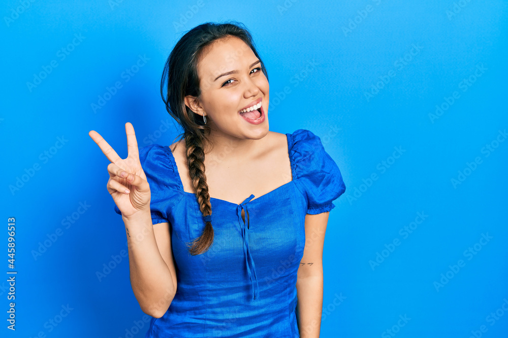 Young hispanic girl wearing casual clothes smiling with happy face winking at the camera doing victory sign. number two. Young hispanic girl wearing casual clothes smiling with happy face winking at the camera doing victory sign. number two.